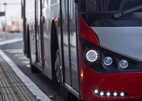 Red and gray bus with bright headlights, parked on the street.