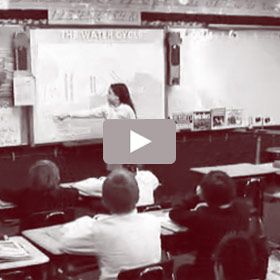 Teacher pointing at a whiteboard, lecturing to students in a classroom about the water cycle.