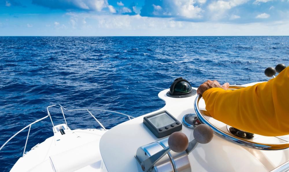 A Man Is Steering A Boat In The Ocean — PASMA Electrical In Cooktown, QLD
