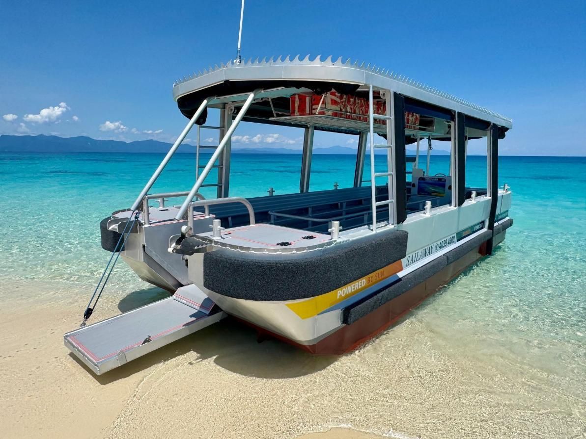 Pontoon boat with ramp on a beach, turquoise water, blue sky, aluminum frame, seats, and side safety bumpers - — PASMA Electrical In Portsmith, QLD