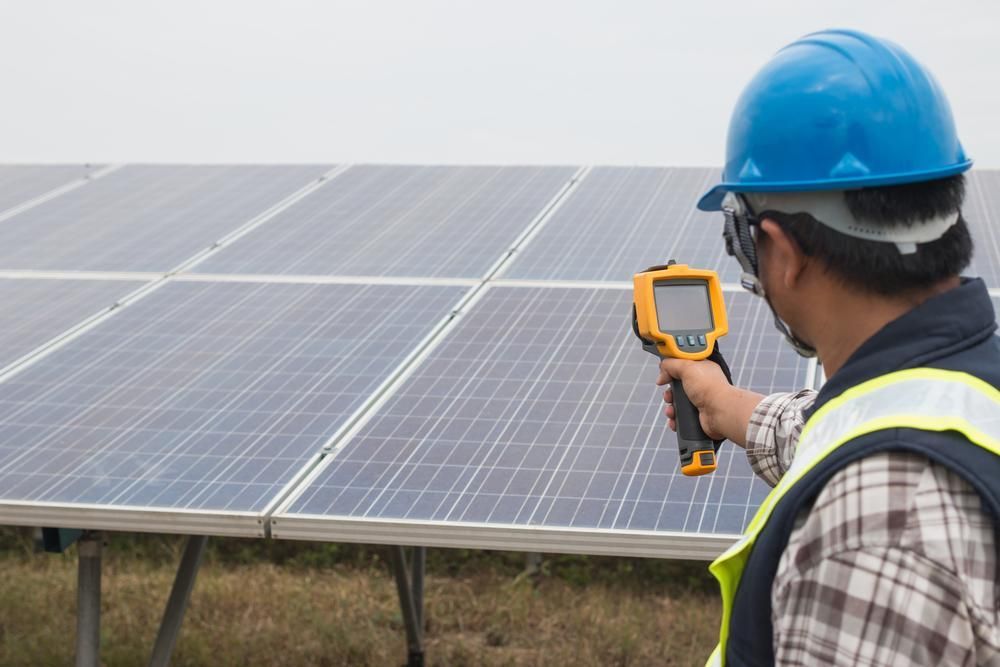 A Man Is Holding A Thermometer In Front Of A Solar Panel — PASMA Electrical In Weipa, QLD