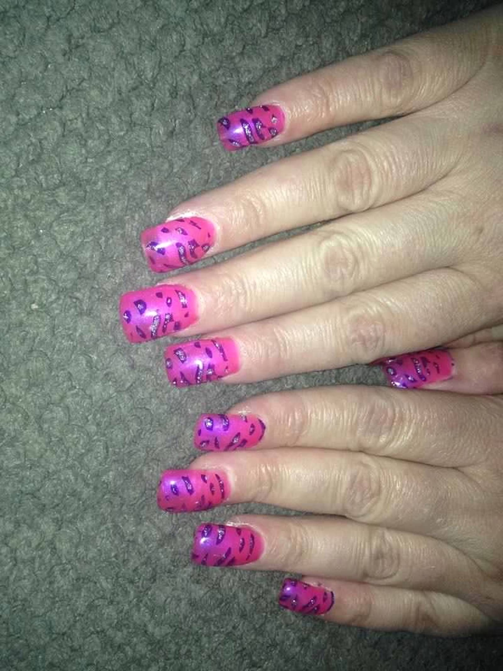 Hands with bright pink patterned nail polish on a green carpet background
