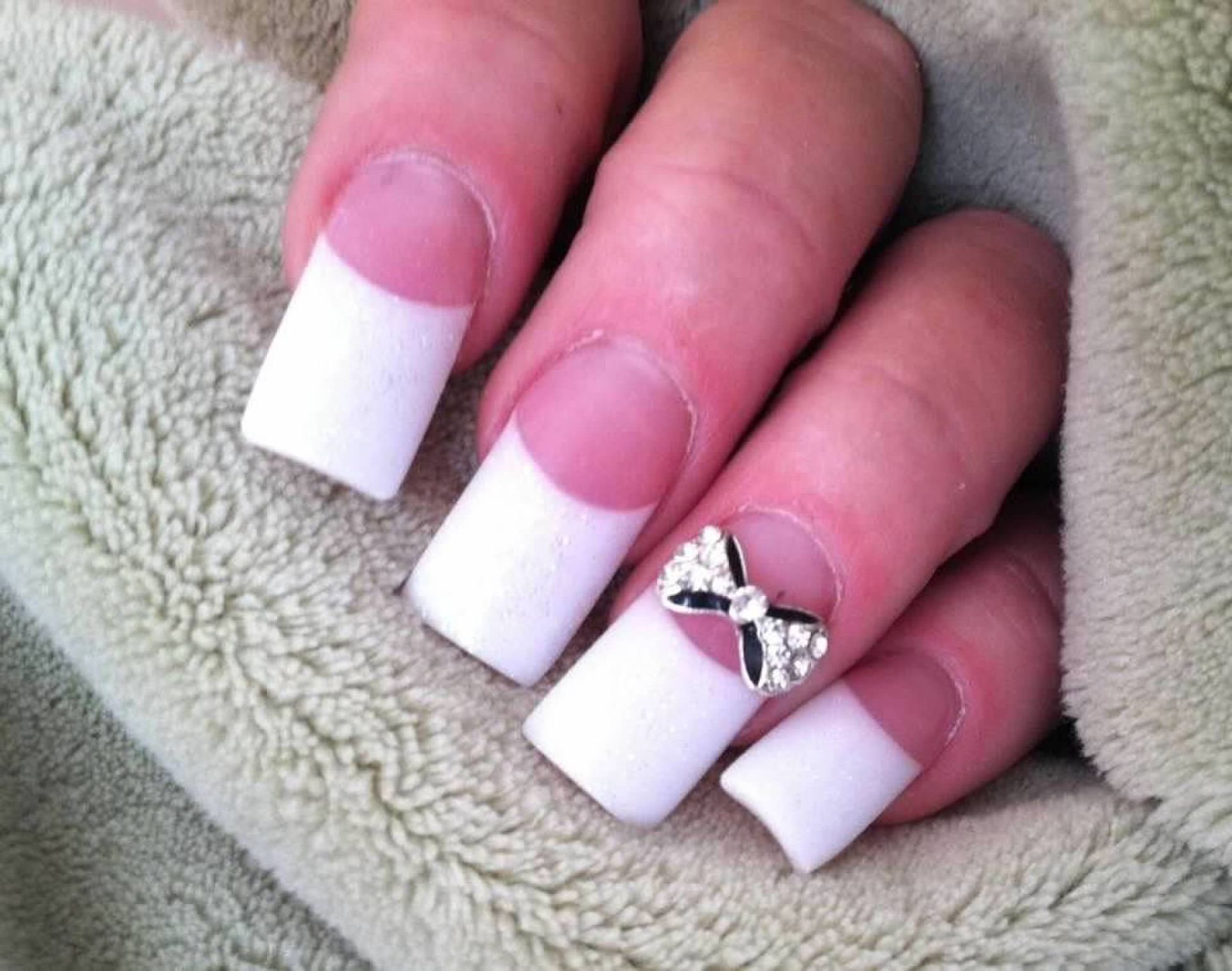 Manicured hand with white French tips and a silver bow accent nail on a soft blanket
