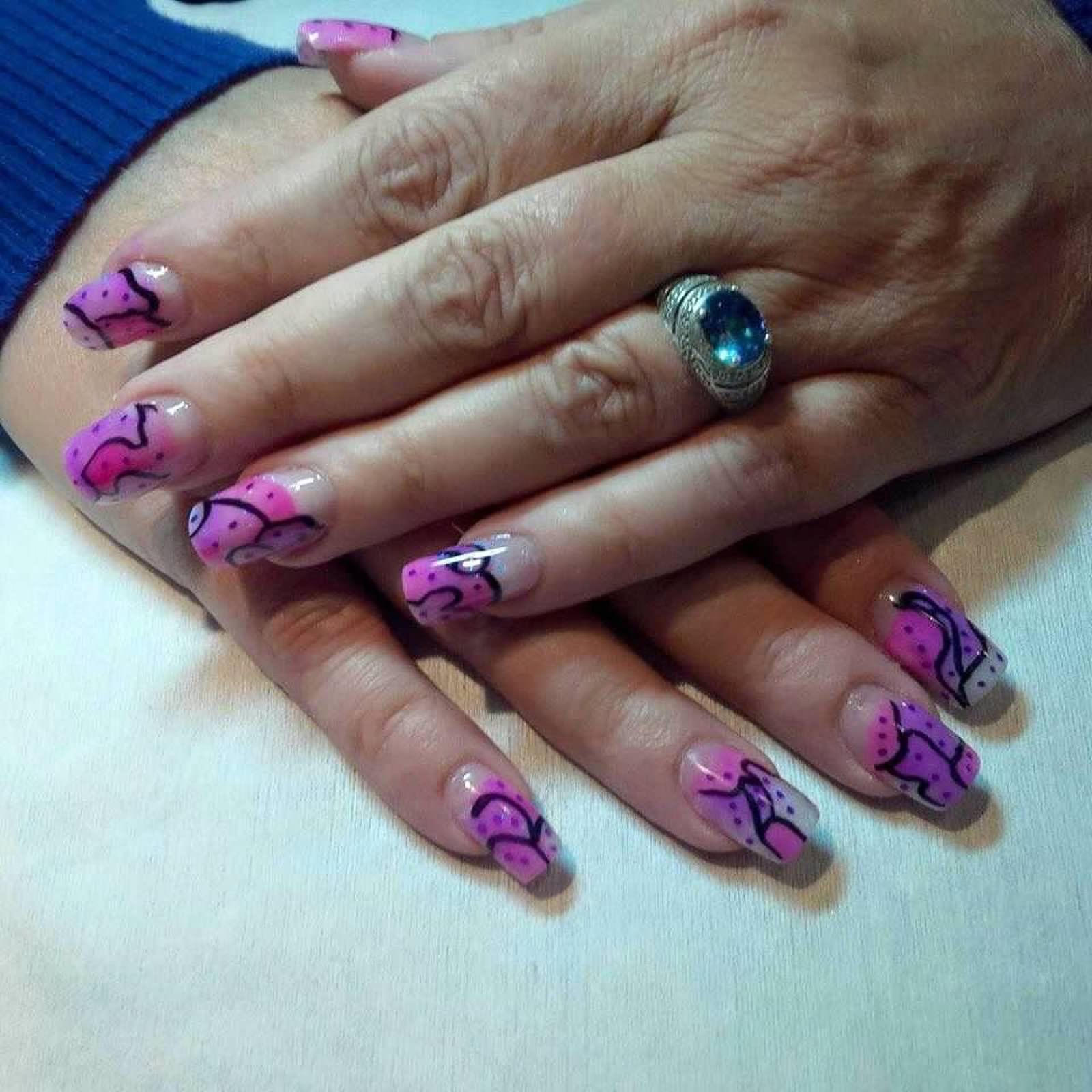Hands with pink and black nail art resting on a white surface, wearing a blue sleeve and a silver ring