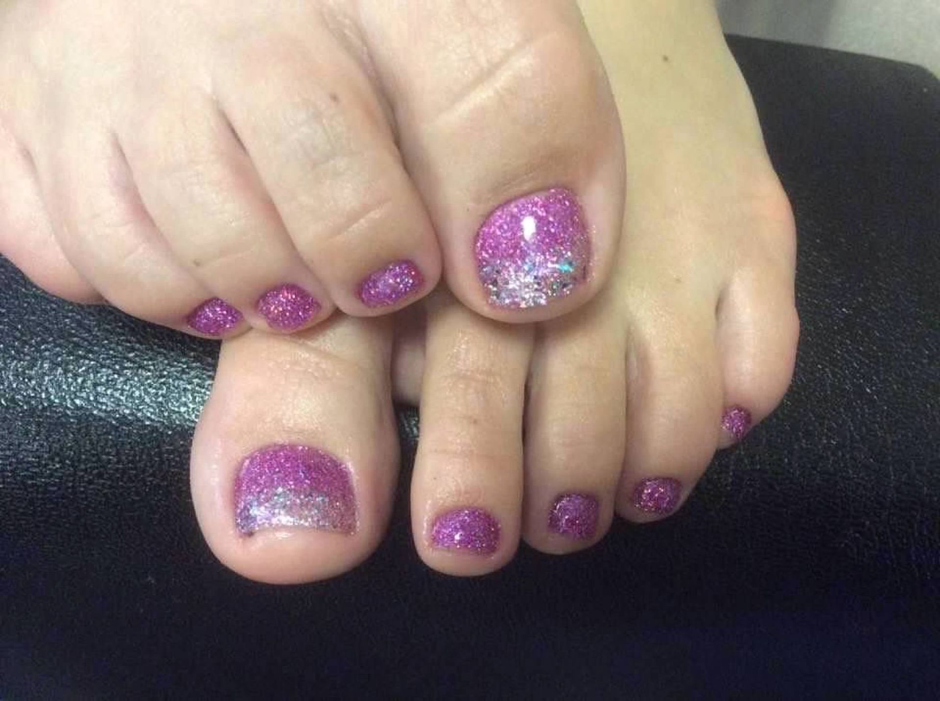 Close-up of feet with sparkly pink-purple glitter nail polish on toenails.