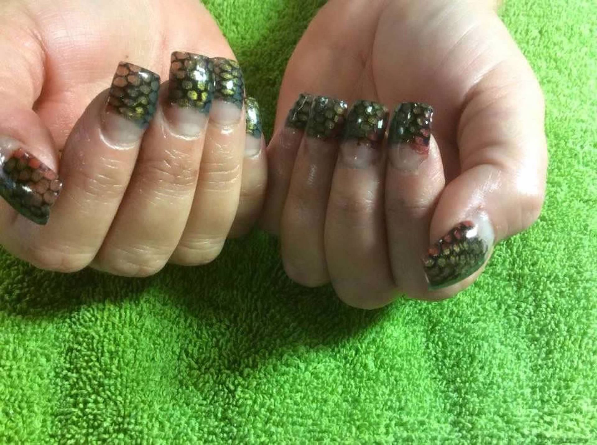 Hands with dark green patterned nail art on a bright green textured surface