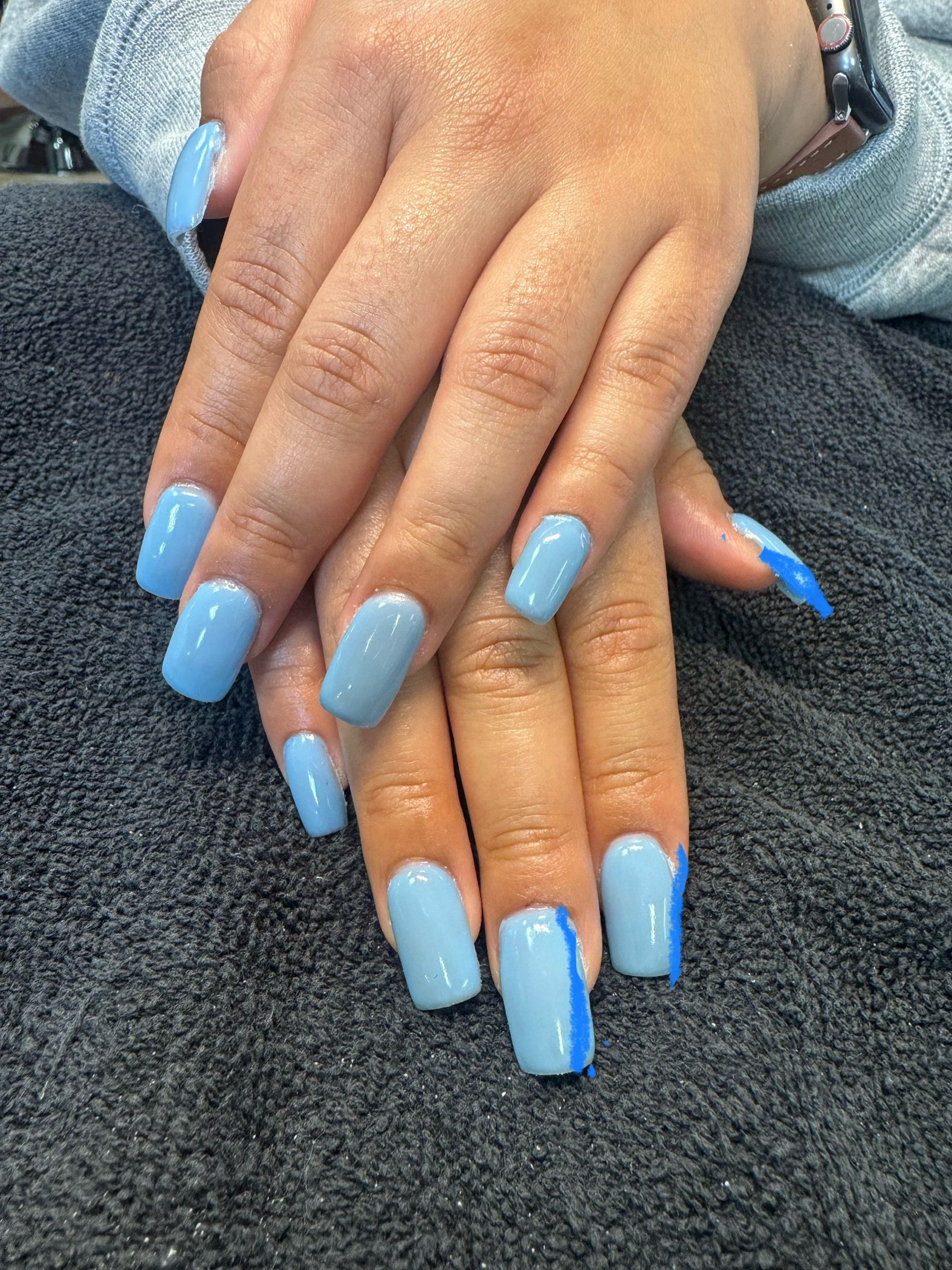 Manicured hands with long glossy light-blue nails resting on a dark towel