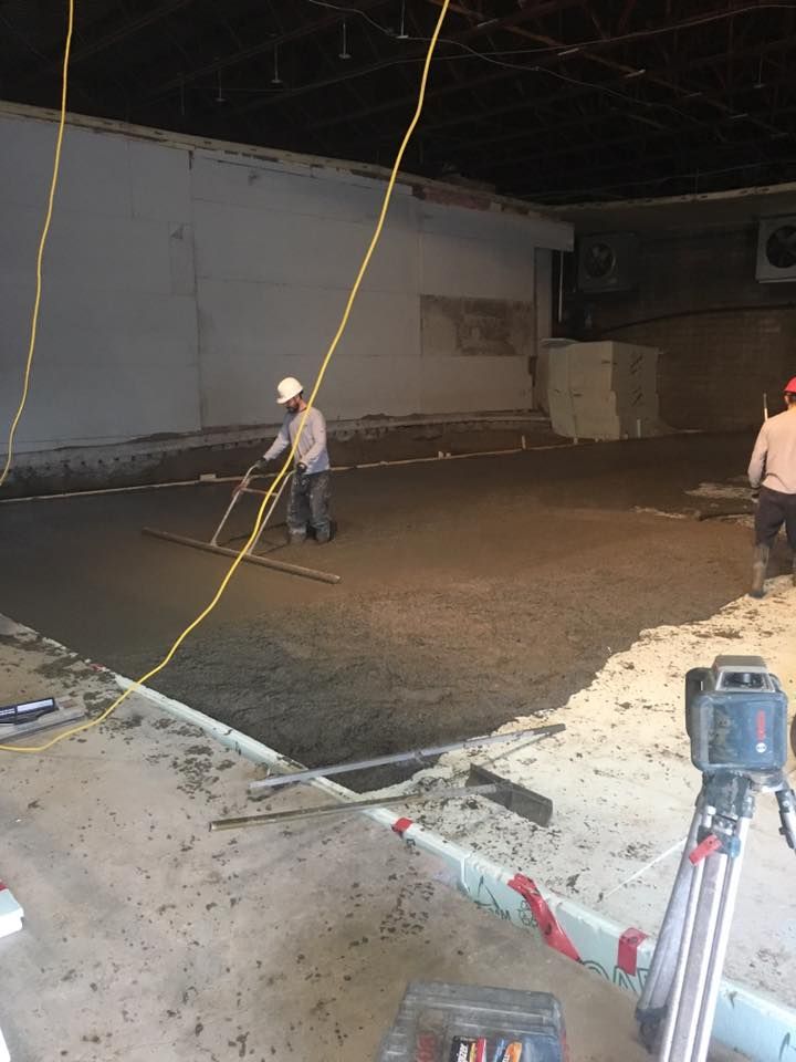 Des ouvriers du bâtiment nivellent un sol en béton humide dans une pièce, à l'aide d'outils et d'équipements.
