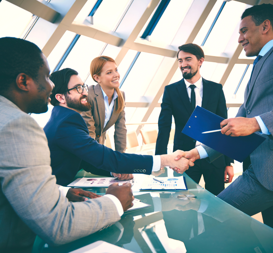 a group of business people are sitting around a table shaking hands