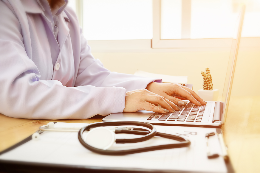 a doctor is typing on a laptop computer next to a stethoscope .