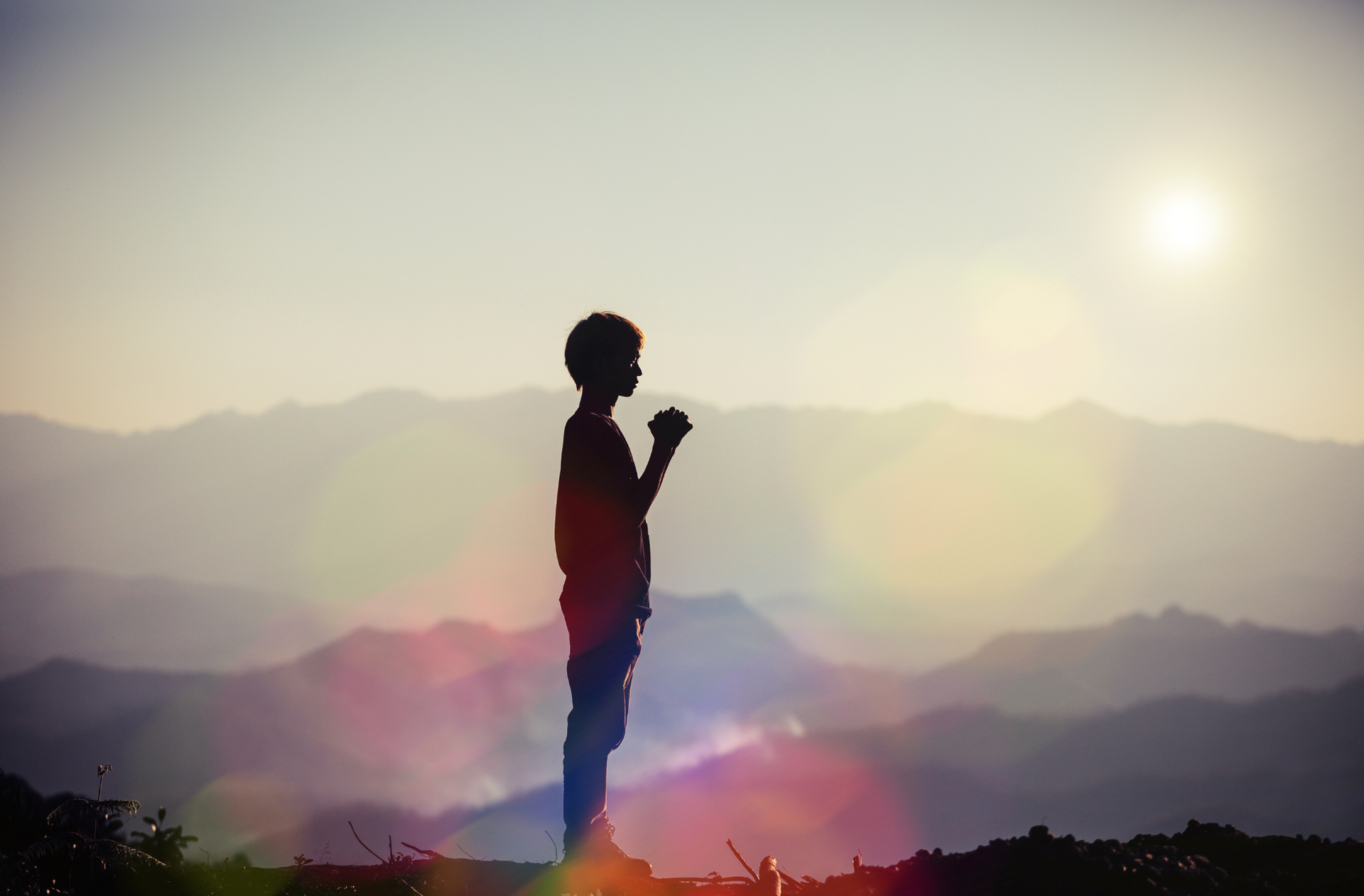 a silhouette of a boy praying on top of a mountain .