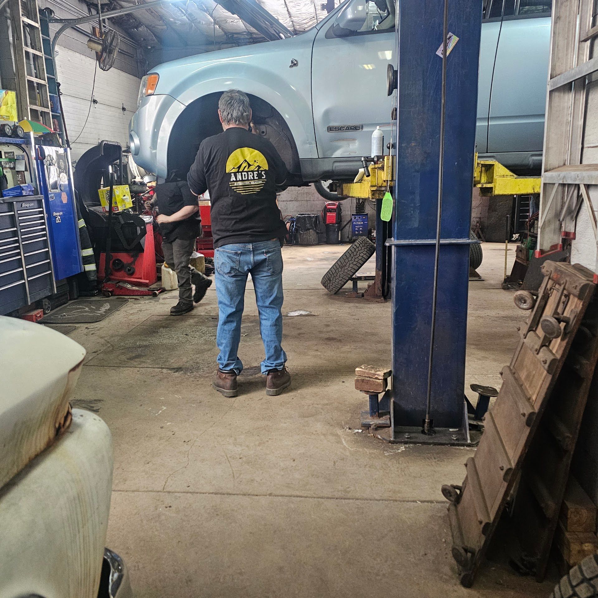 Mechanic shop with a lifted blue car and two people working underneath on jack stands Check Mark | Andre's Automotive Solutions LLC
