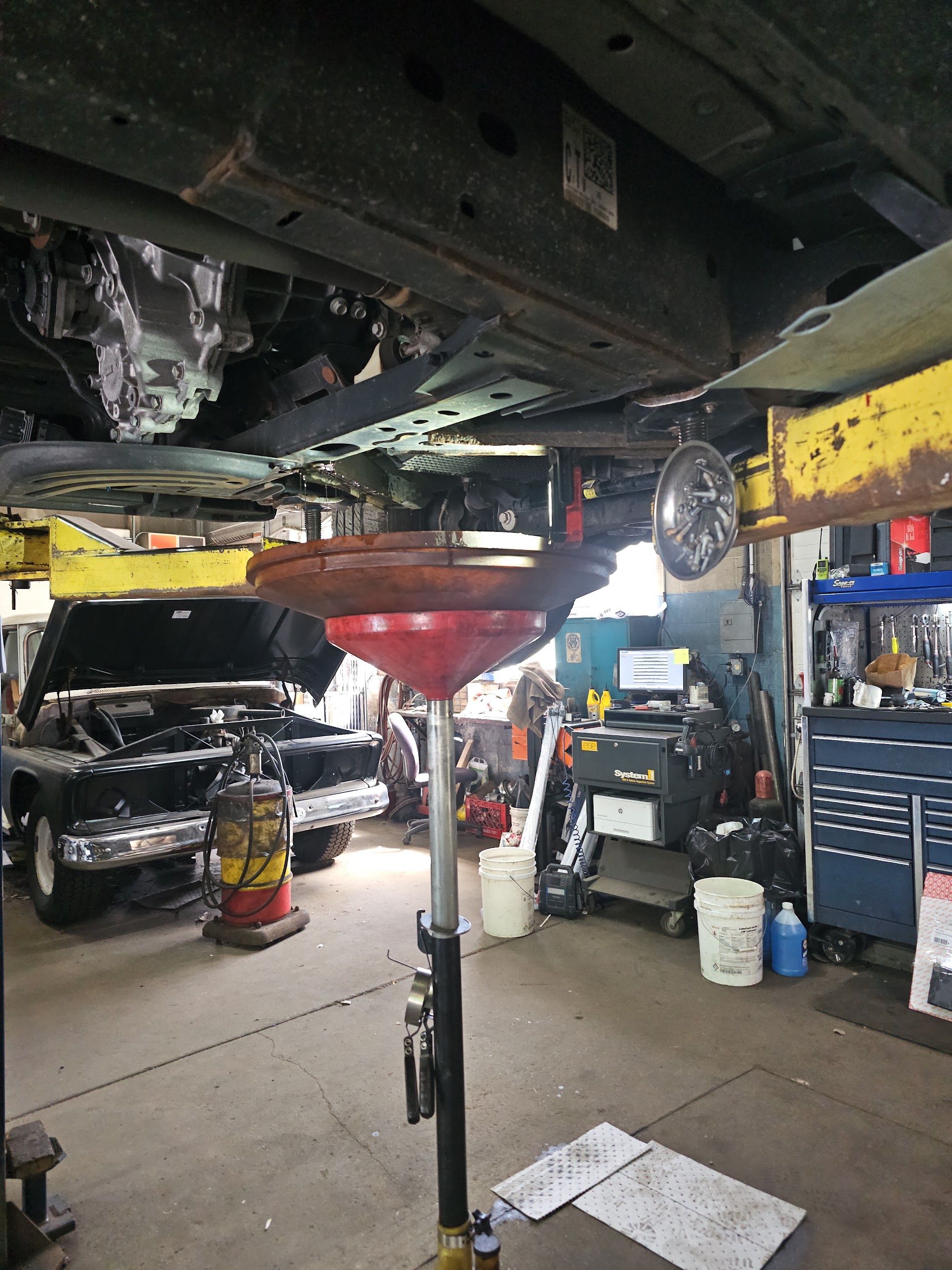 Auto repair shop with a car on a lift, a red oil drain pan, and tools in a garage. | Andre's Automotive Solutions LLC