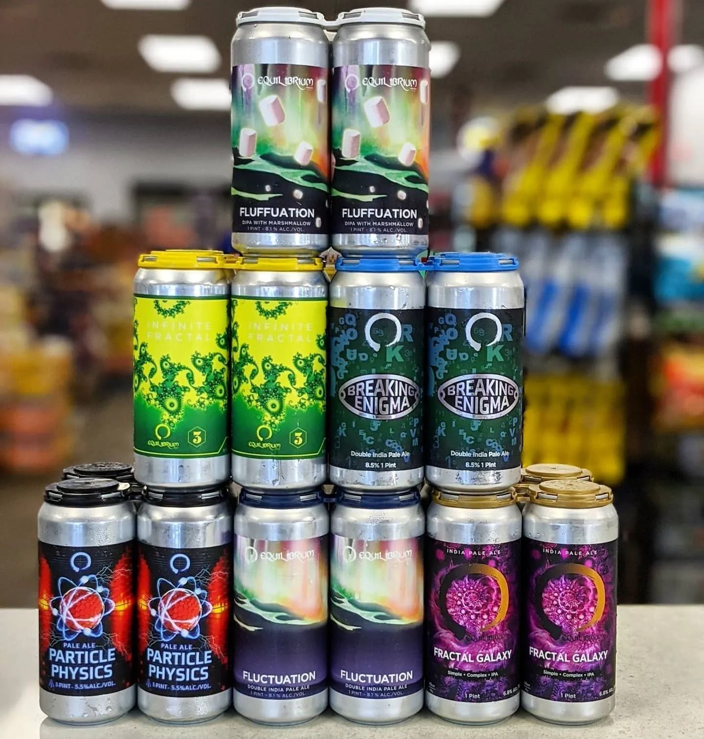 A pyramid of colorful beer cans on a counter in a store. Labels have science-themed names.
