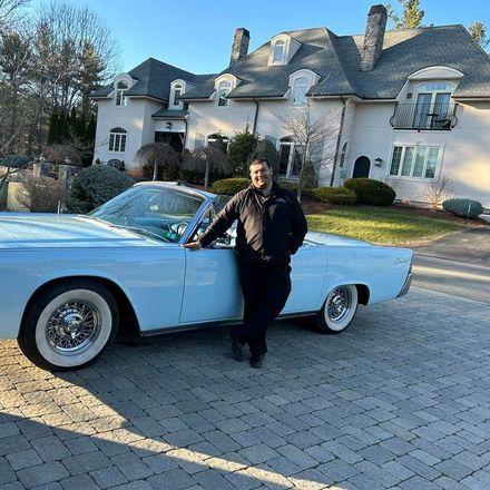 A man is standing next to a white car in front of a house.