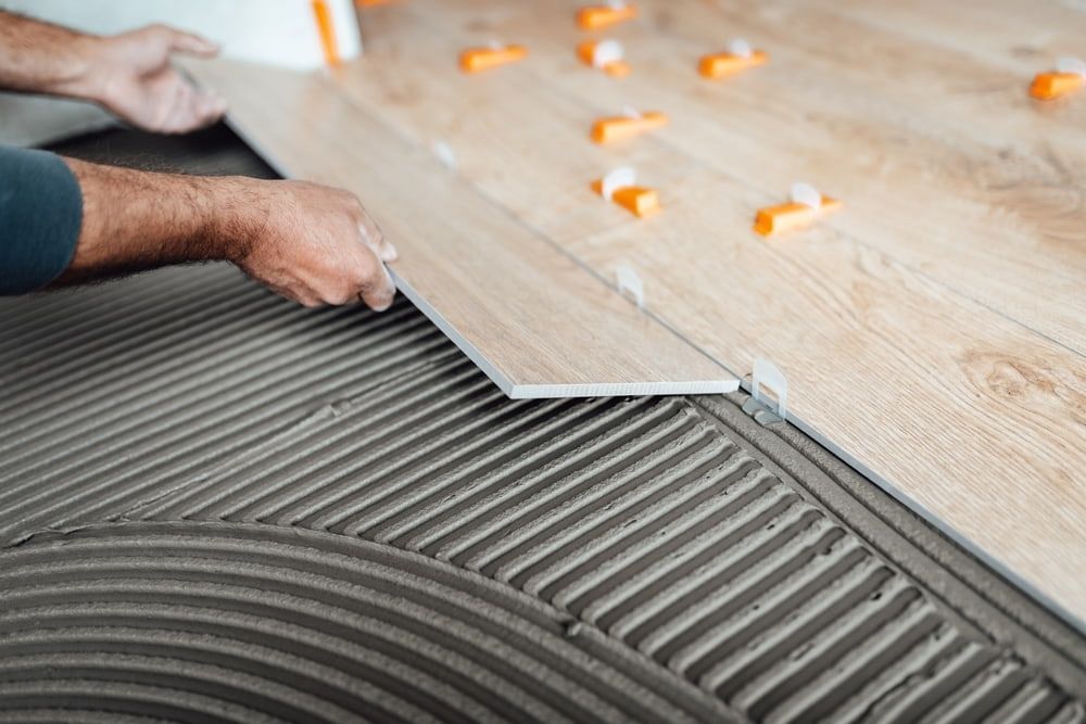 A Man is Laying a Tile on a Wooden Floor — Northern Tile Gallery in Winnellie, NT