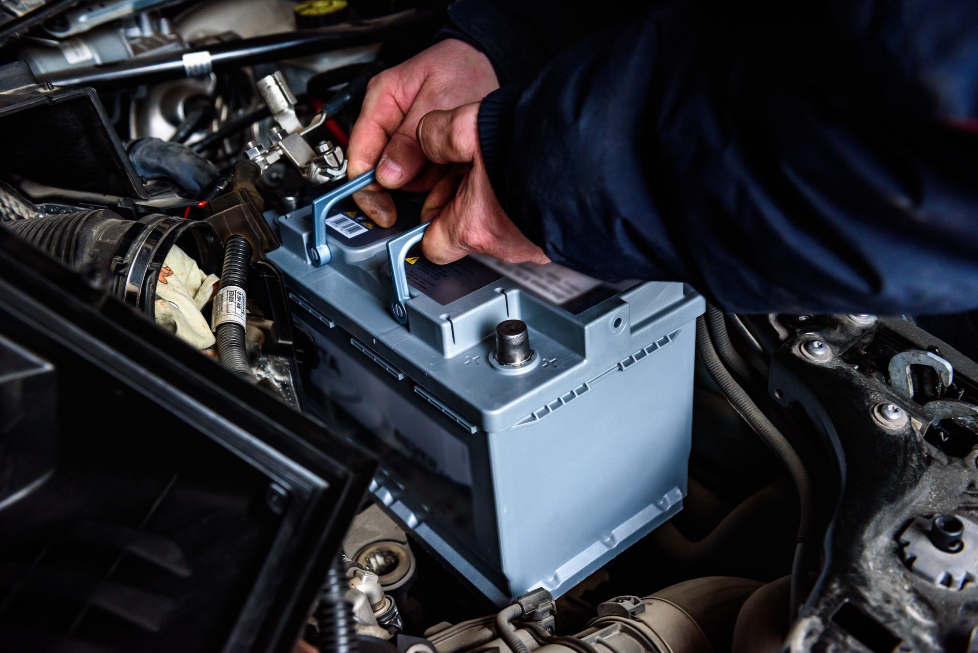 Hands installing a gray car battery in a vehicle engine bay Hands installing a gray car battery in a vehicle engine bay
