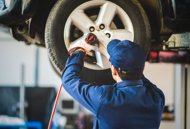 Mechanic using a wrench on a raised car wheel in an auto shop