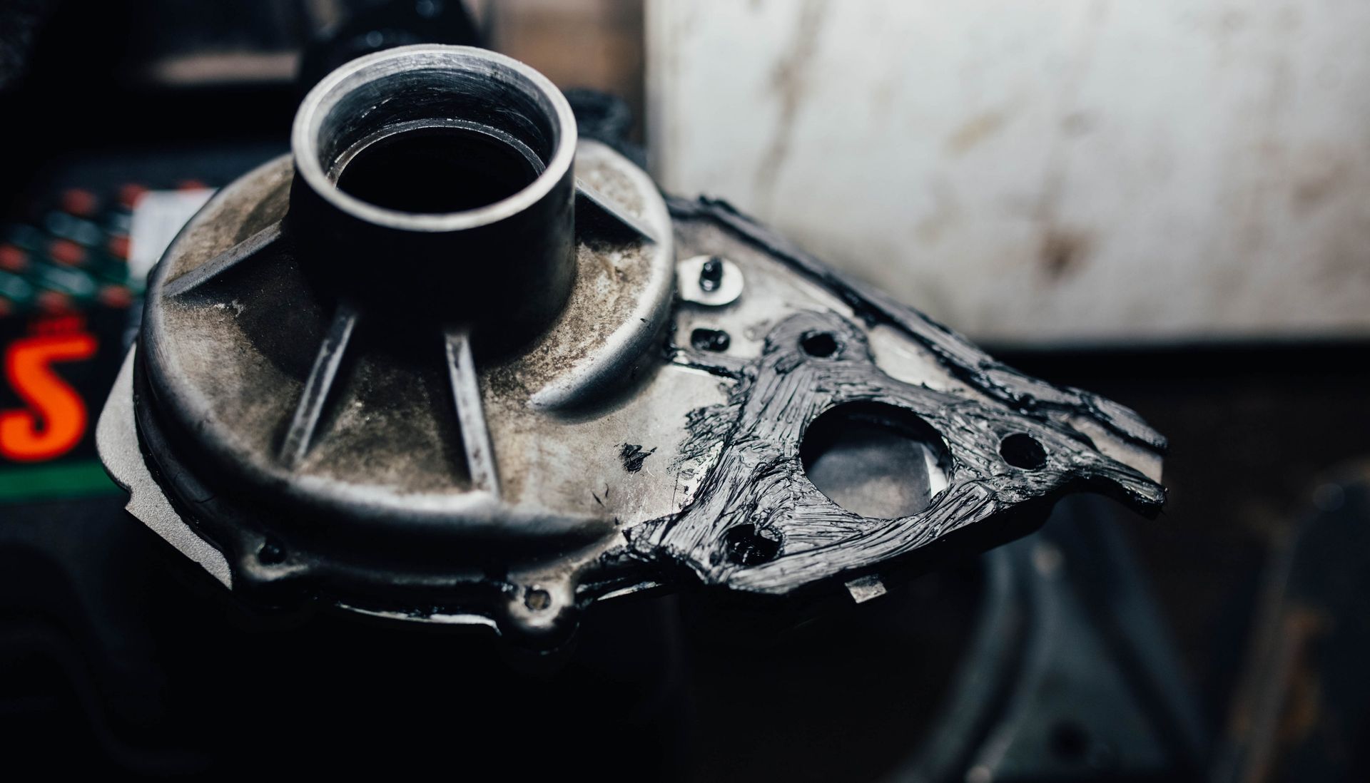 Close-up of a damaged black metal mechanical part with bolts on a dark surface