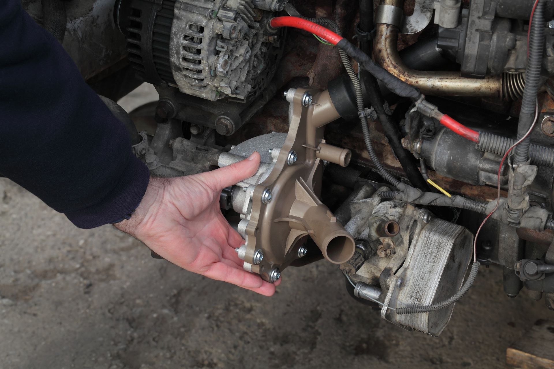 Hand holding a metal engine component near a vehicle engine bay in a garage