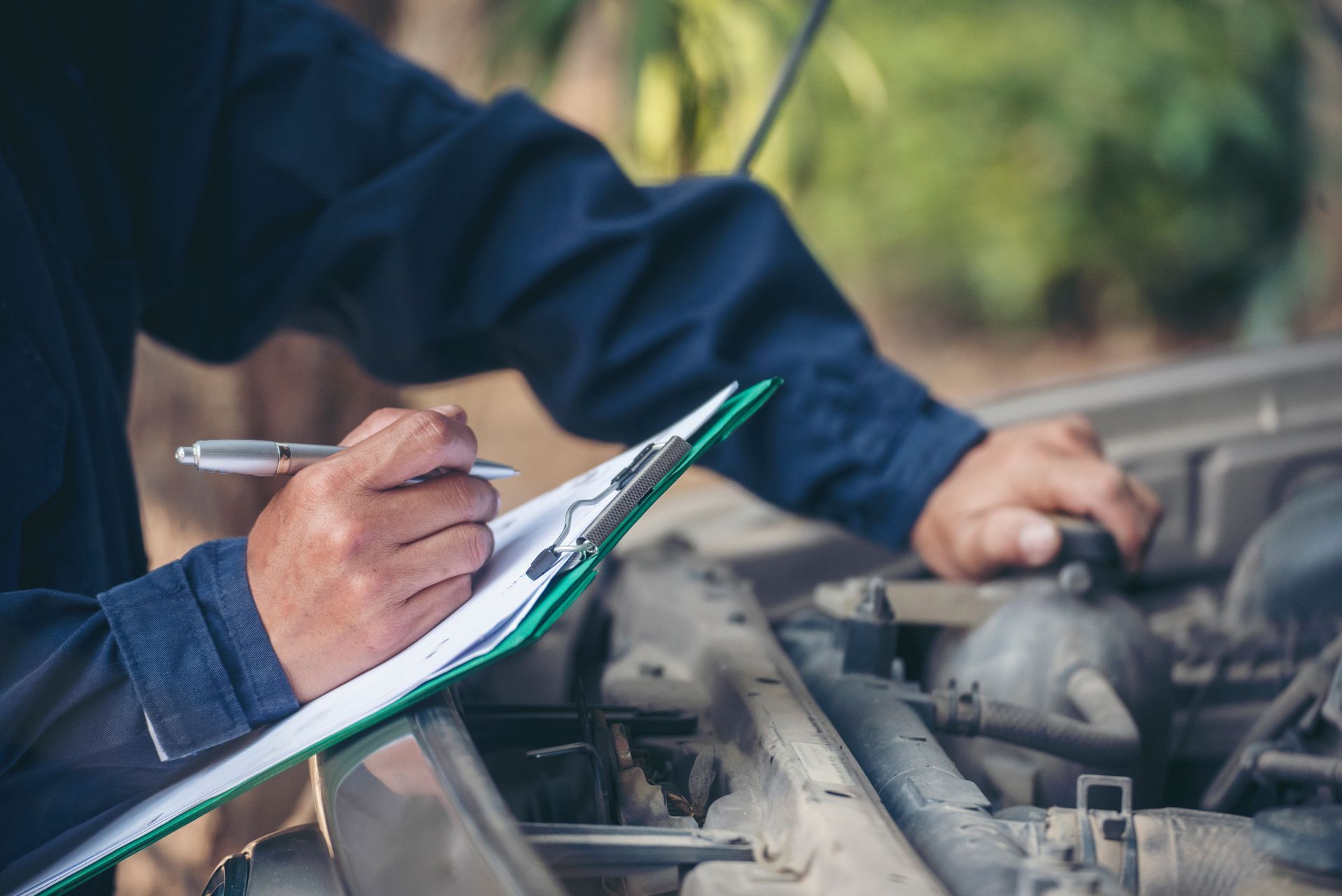 Mechanic writing notes while inspecting a car engine under the hood Mechanic writing notes while inspecting a car engine under the hood