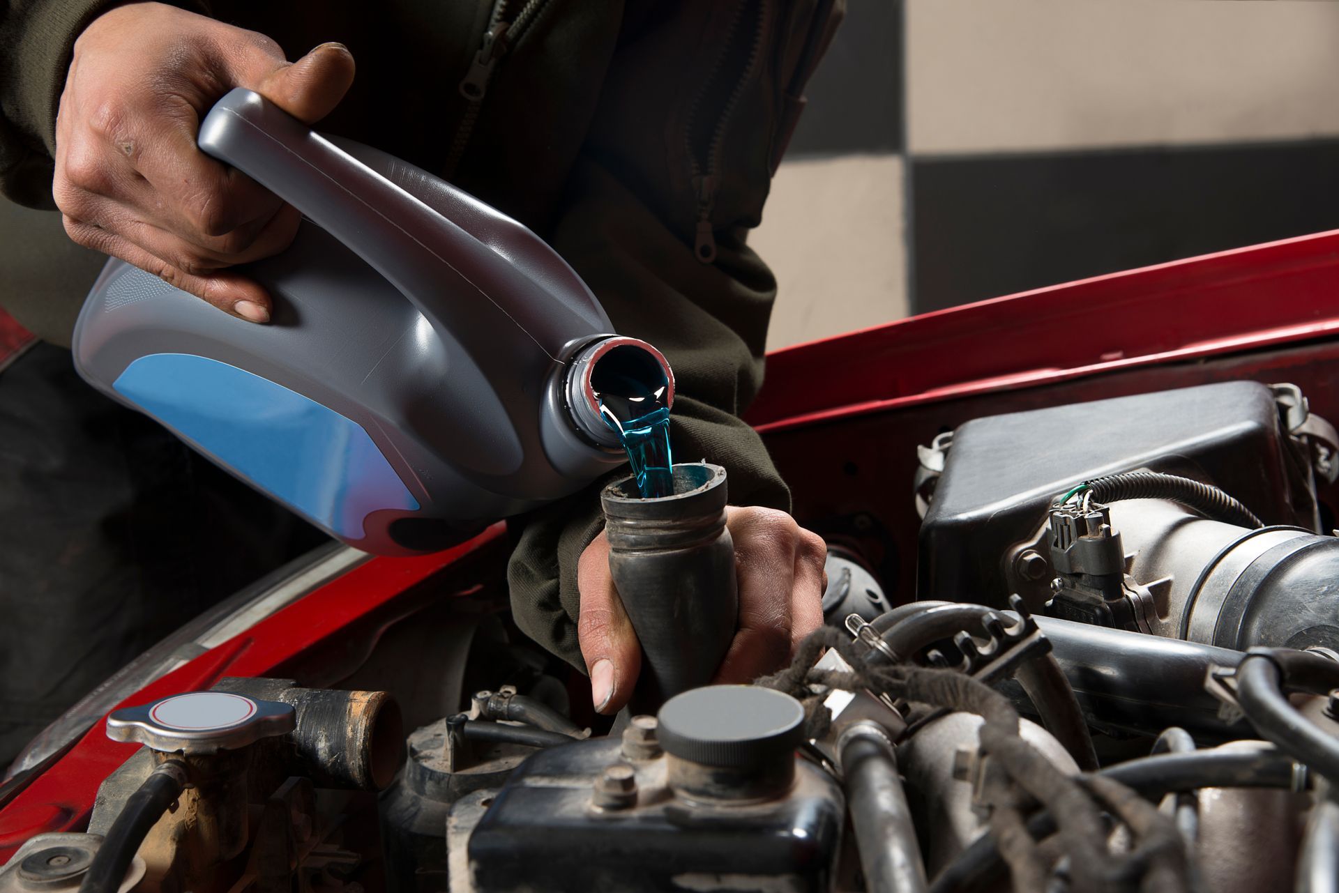 Person pouring blue fluid into a car engine reservoir in an auto repair shop Person pouring blue fluid into a car engine reservoir in an auto repair shop