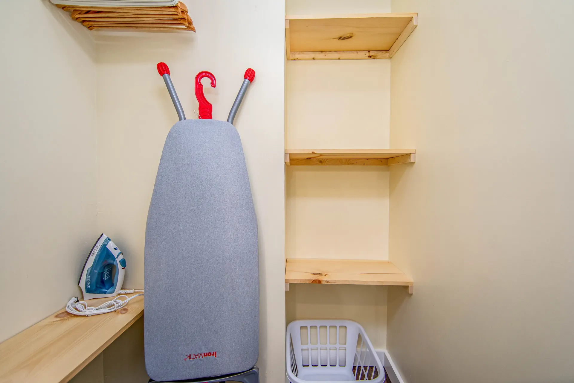 A laundry room with an ironing board and a laundry basket.