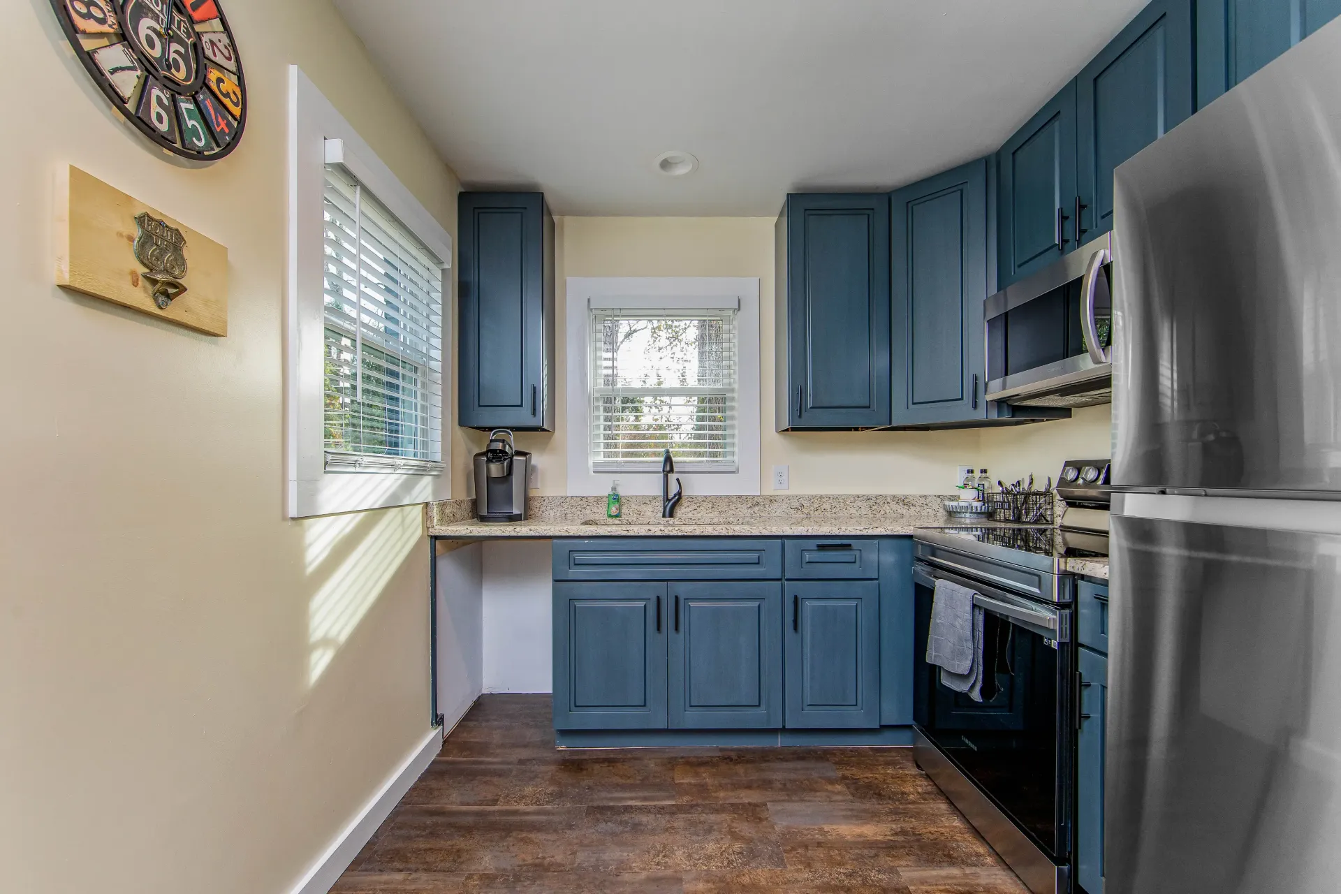 A kitchen with blue cabinets , stainless steel appliances , and a clock on the wall.
