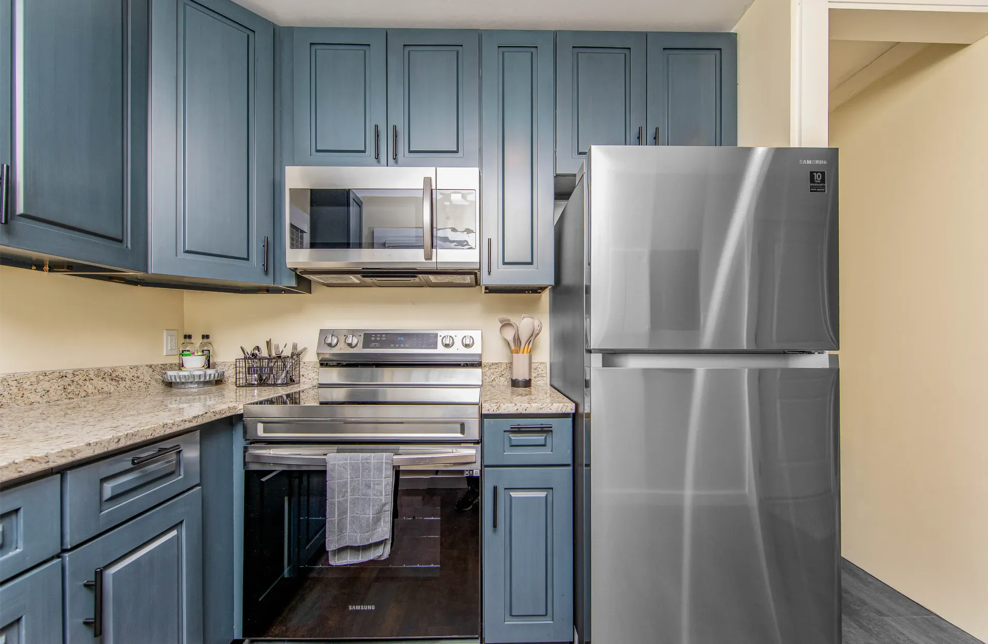 A kitchen with blue cabinets , a stainless steel refrigerator , a stove , and a microwave.