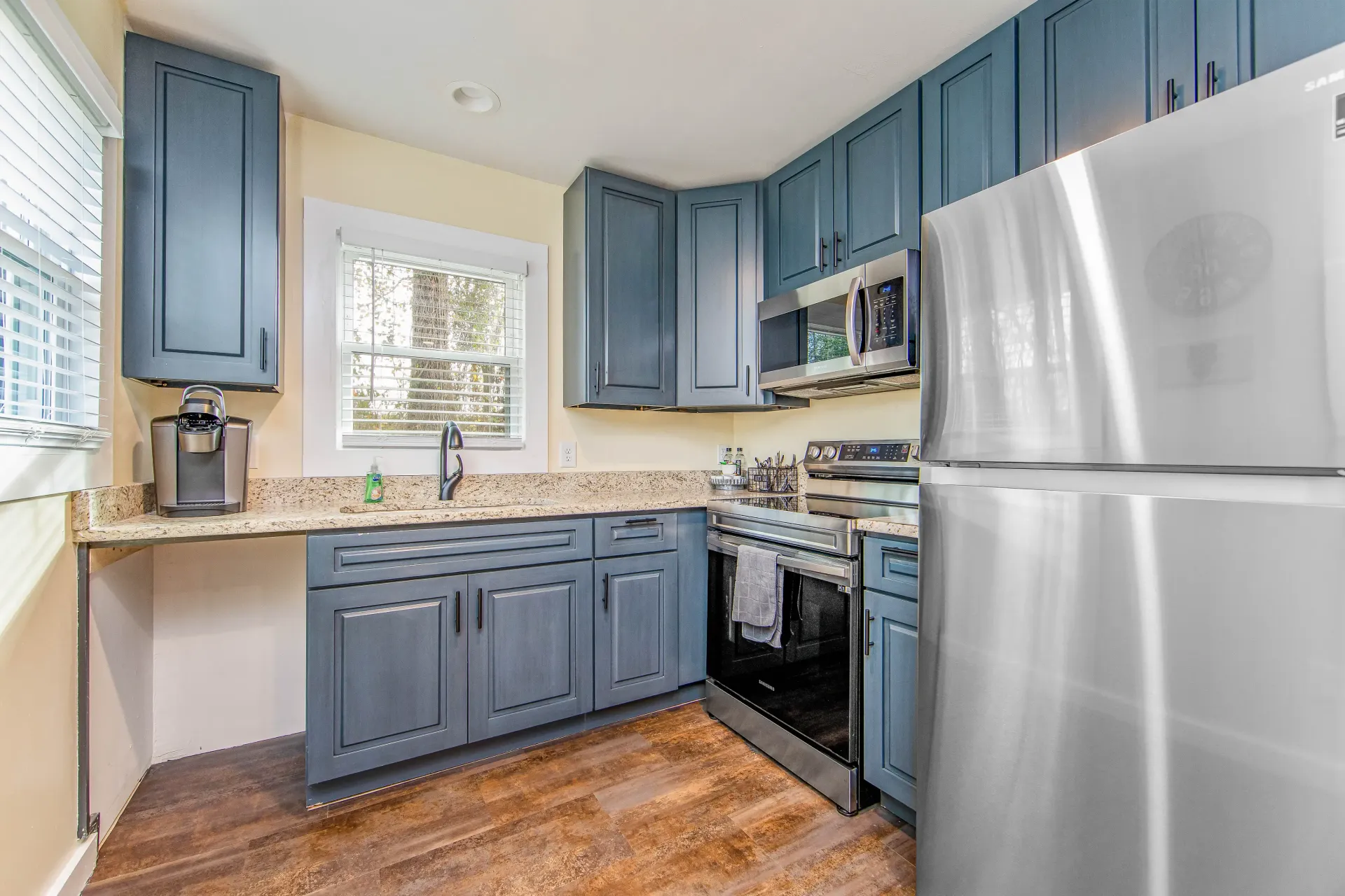 A kitchen with blue cabinets , stainless steel appliances , and a stainless steel refrigerator.