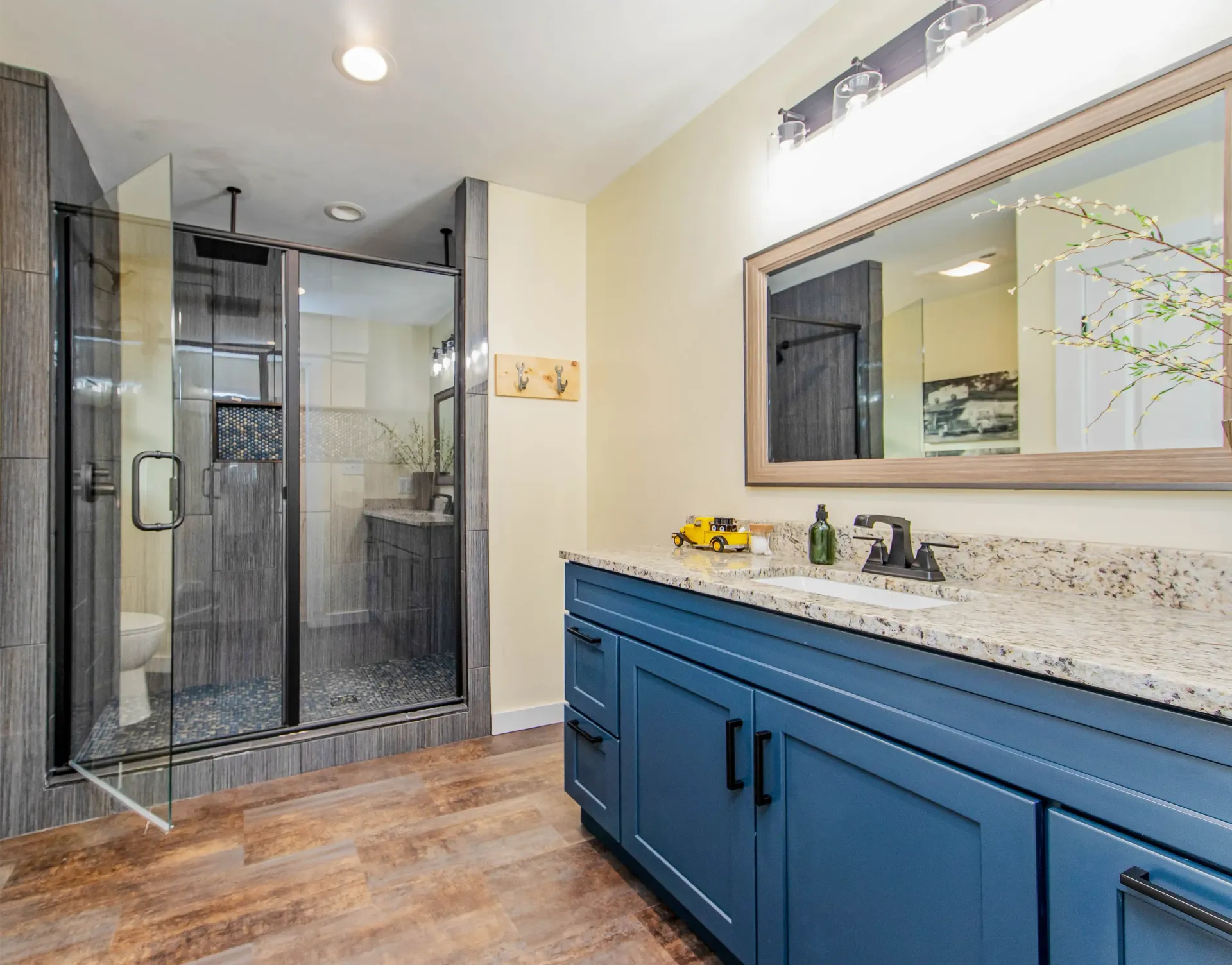 A bathroom with blue cabinets , granite counter tops , a walk in shower and a large mirror.