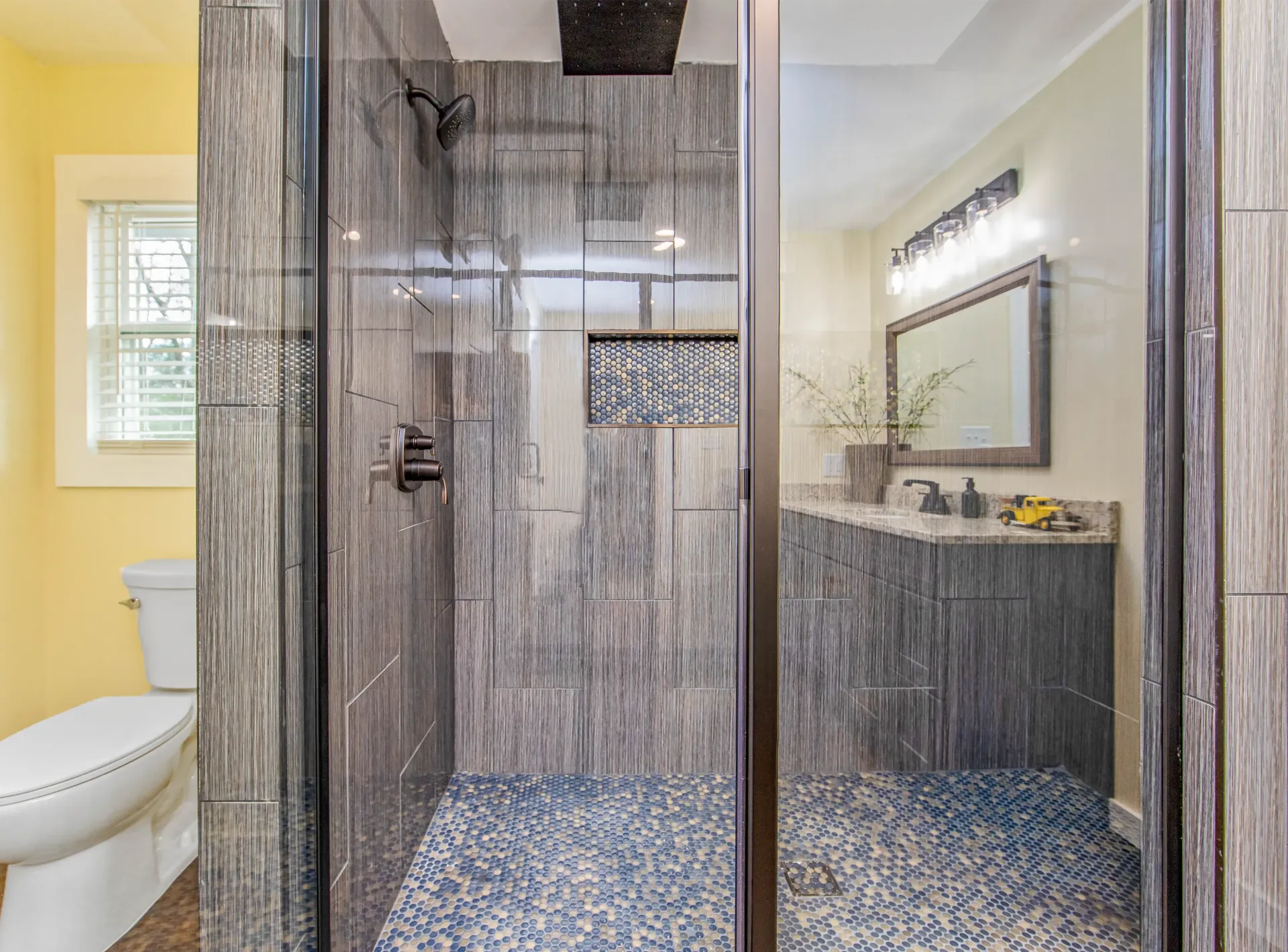 A bathroom with a walk in shower , toilet , sink and mirror.