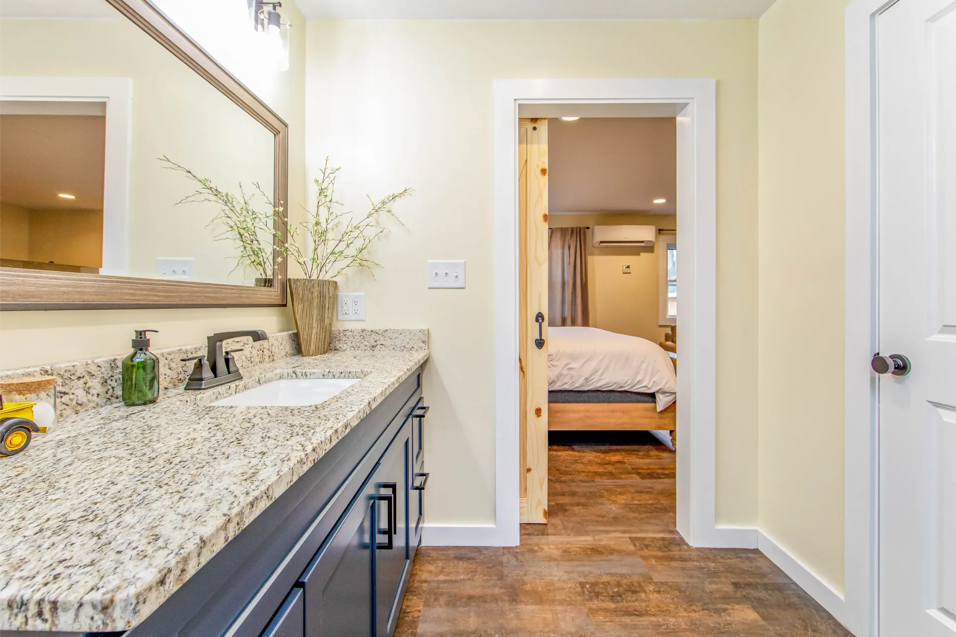 A bathroom with a sink , mirror , and cabinets leading to a bedroom.