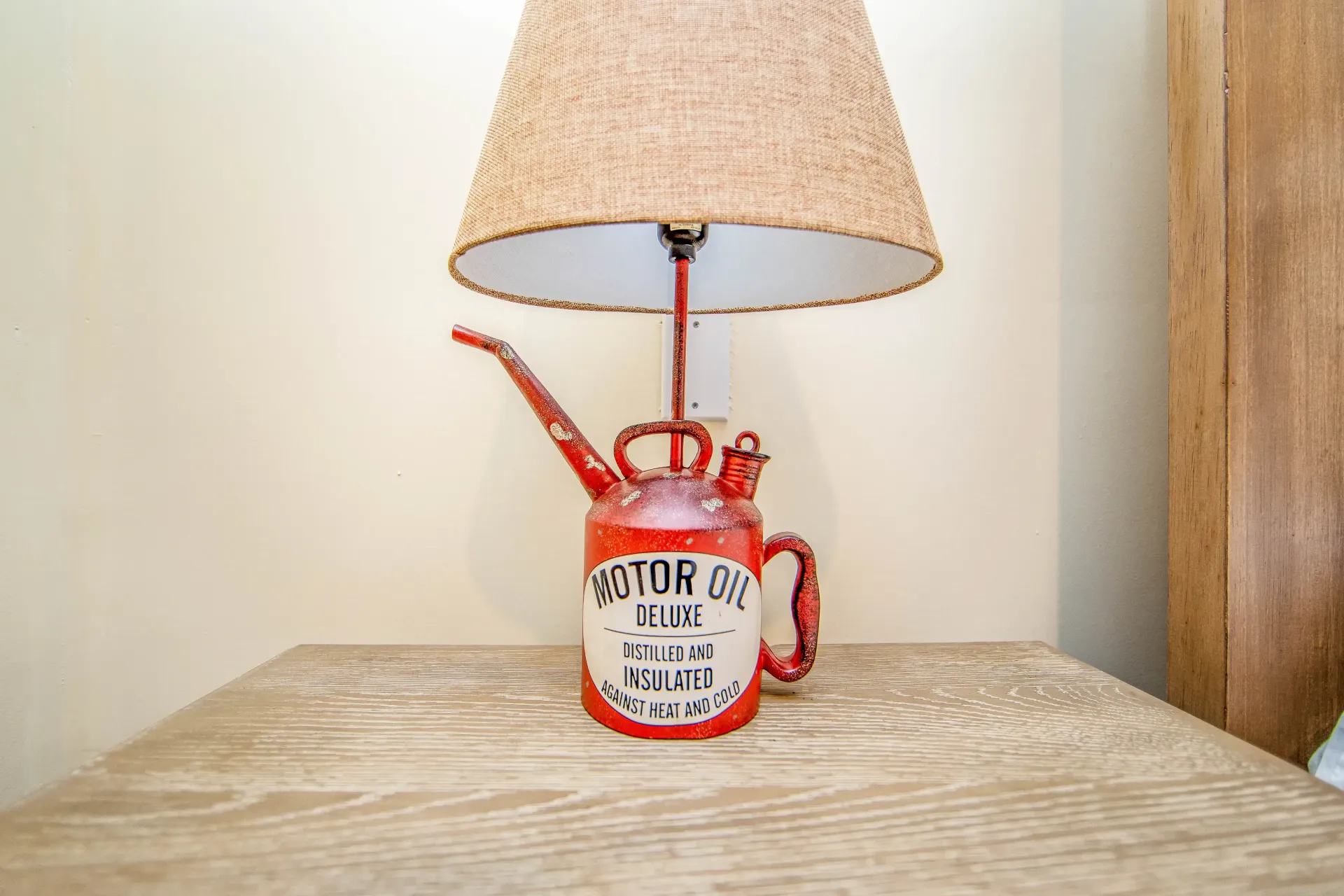 A lamp made out of a red oil can is sitting on a wooden table.