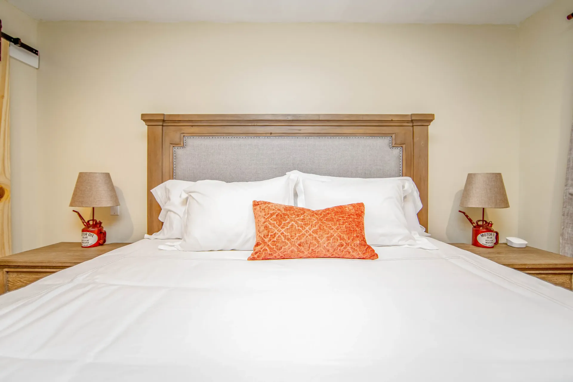 A bed with white sheets and orange pillows in a bedroom.