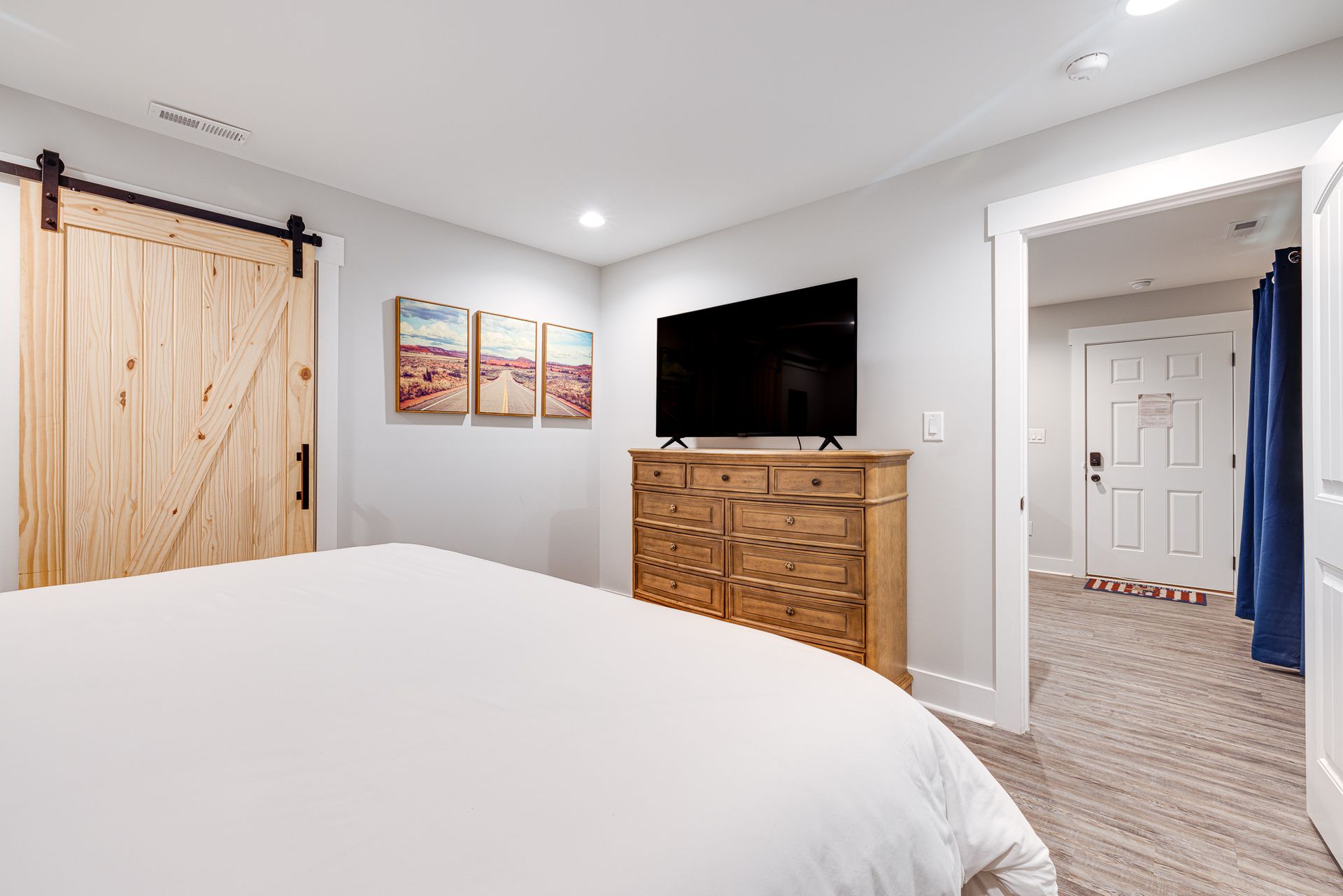 A bedroom with a bed , dresser , television and sliding barn doors.