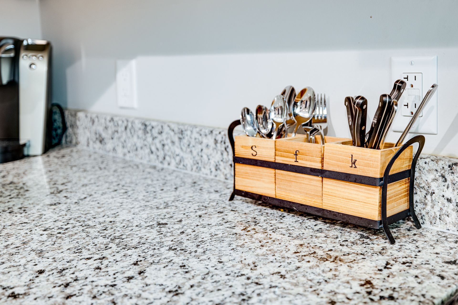 A wooden utensil holder is sitting on a granite counter.