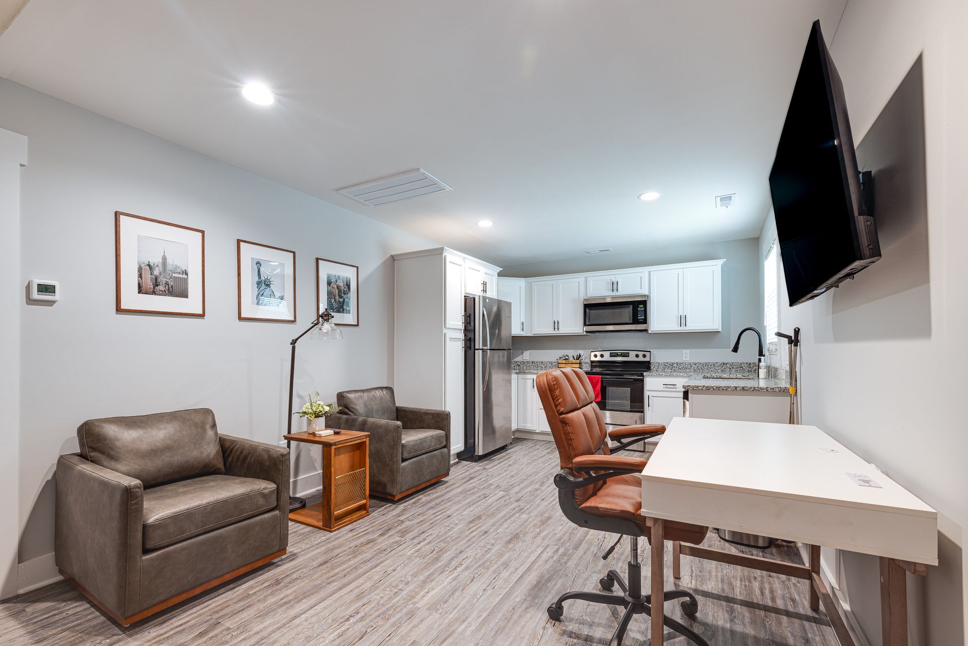 A living room with two chairs , a desk and a flat screen tv.
