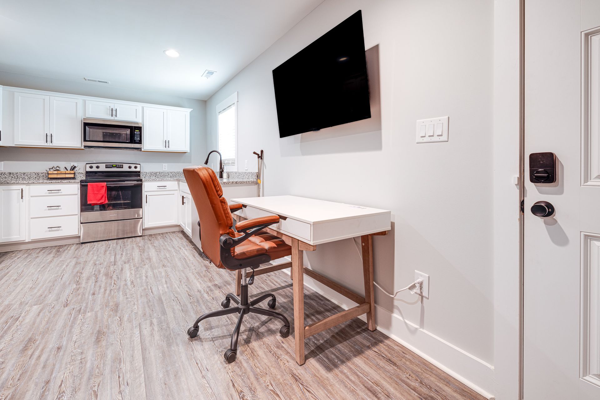A kitchen with a desk and chair and a flat screen tv on the wall.
