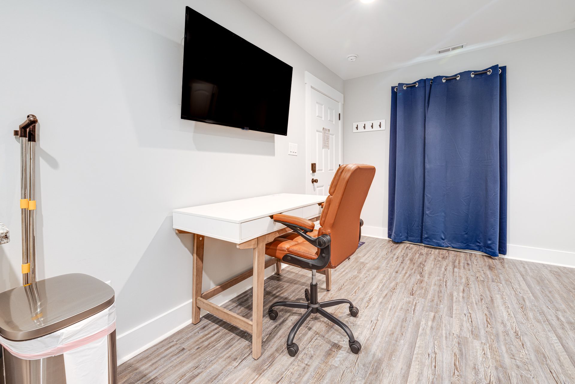 A room with a desk , chair , television and trash can.