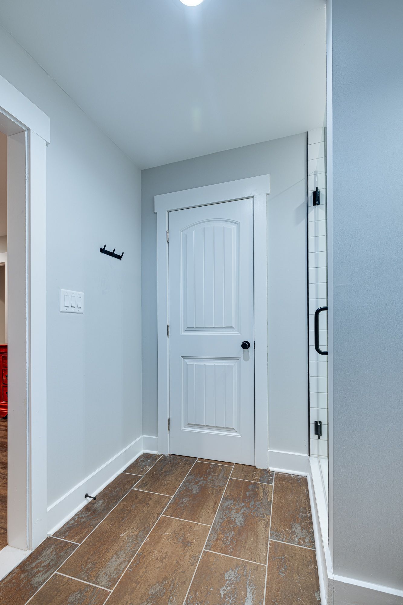A hallway with a white door and a brown tile floor.