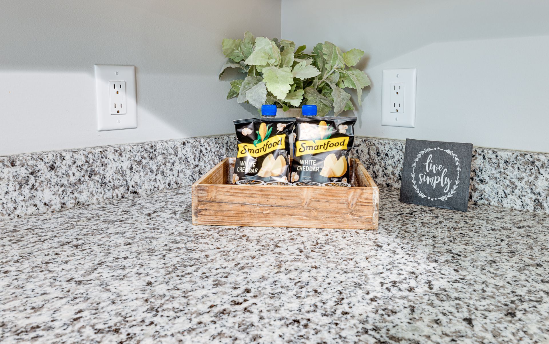 A wooden tray filled with snacks is on a granite counter.