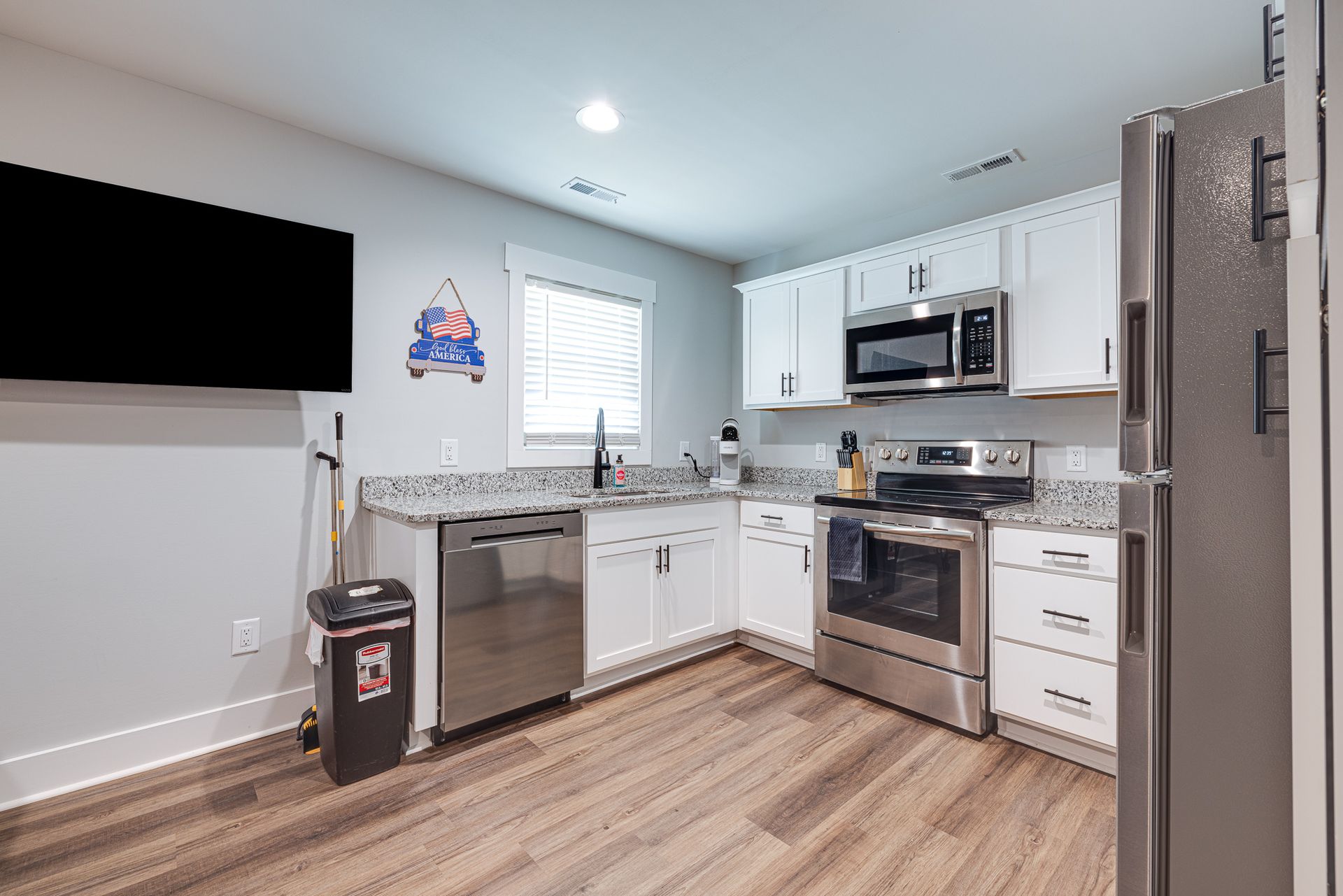 A kitchen with white cabinets , stainless steel appliances and a flat screen tv.