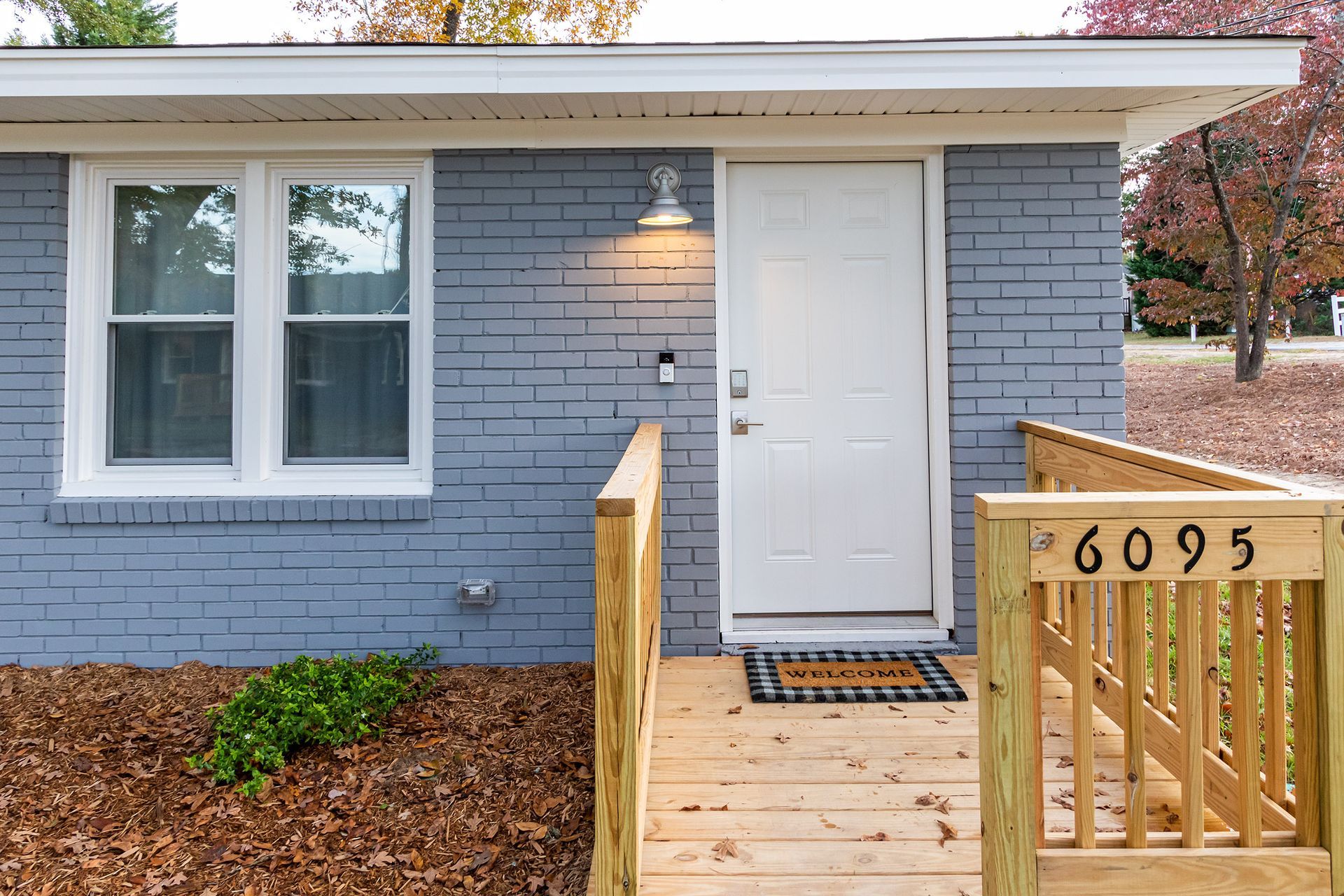 A blue brick house with a white door and a wooden deck