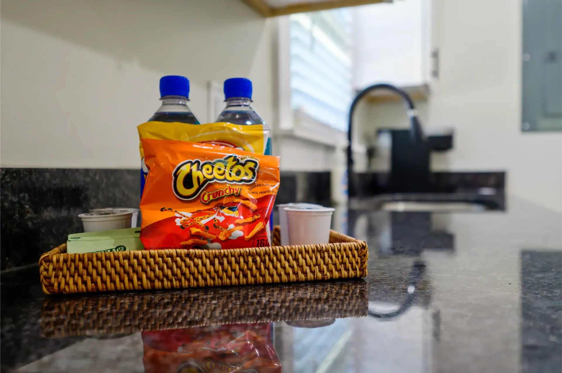 A bag of cheetos is sitting on a wicker tray on a kitchen counter.