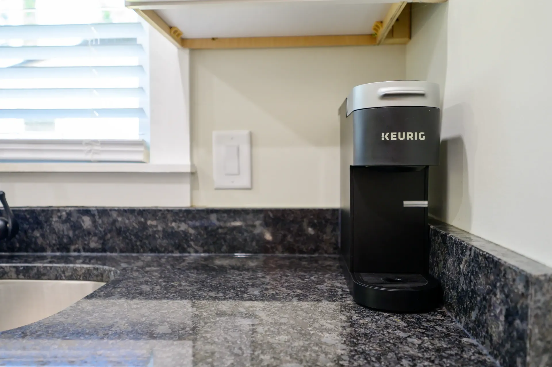 A keurig coffee maker is sitting on a kitchen counter next to a sink.