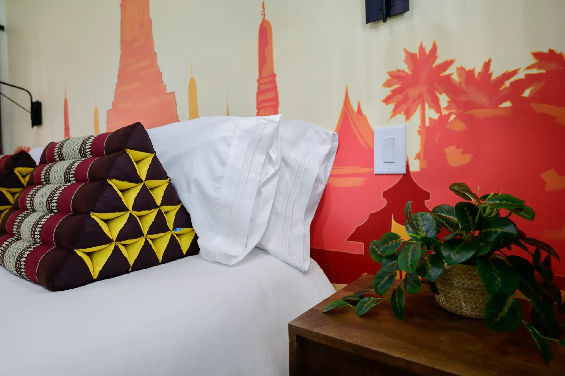 A bed with a plant on a nightstand and a painting on the wall behind it.