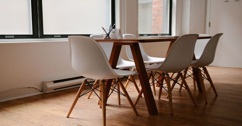 Salle à manger avec table en bois et chaises blanches sur parquet, près d'une fenêtre.