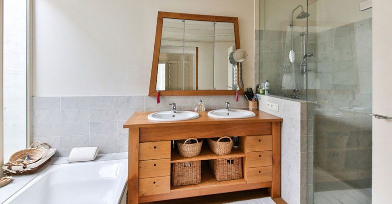 Salle de bains avec meuble-lavabo en bois, double vasque et douche en verre. La baignoire est visible sur la gauche.