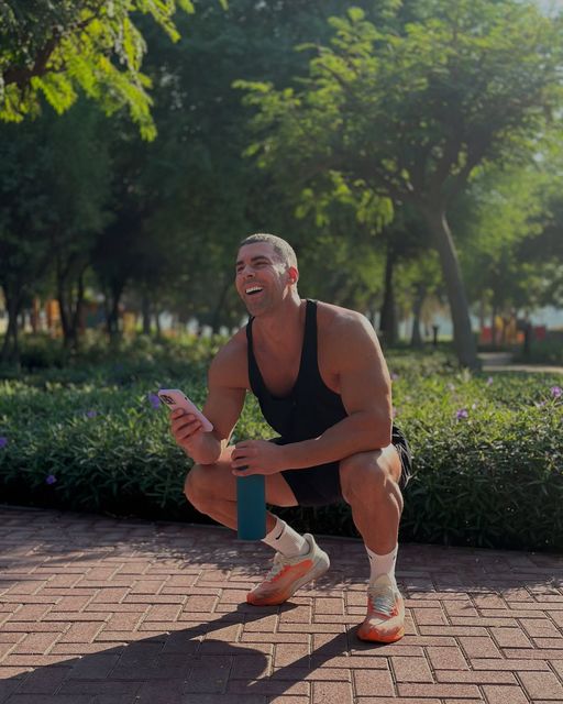 Jay Gardner is squatting down on a brick sidewalk holding a water bottle and a cell phone.